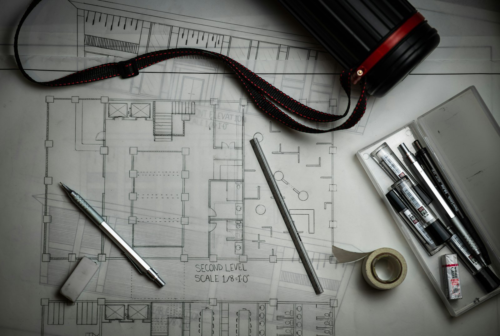 Architectural blueprints with drafting pencils, a ruler and a drawing tube.